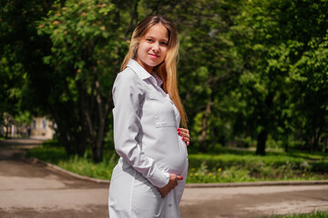 Pregnant young woman smiling and holding hand on belly looking at camera outdoors