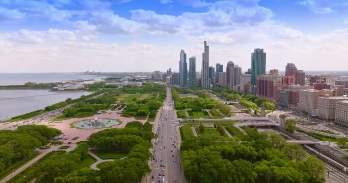 Wide multi-lane road with numerous cars passing through green park zone. Chicago cityscape and skyscrapers at backdrop.