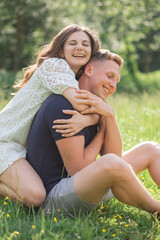 Affectionate young couple sitting on grass in park, embracing. Young man and woman enjoying summer day. 