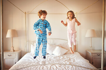 I can jump higher than you. Shot of two young children jumping together on a bed at home.