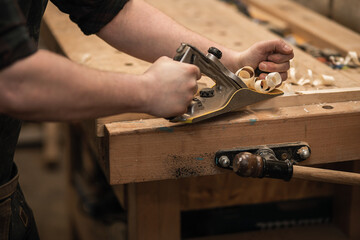 Close-up joiner hands working with wood timber, cutting, sharping by plane, shavings flying around...