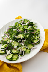 Light summer salad of cucumbers, onions and feta cheese in an oval white dish