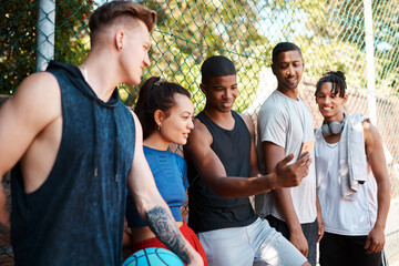 You guys have got to see this. Shot of a group of sporty young people looking at something on a cellphone while standing along a fence outdoors.