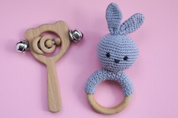 Baby wooden rattle and knitted wooden toy in the form of a rabbit on pink background. Concept of baby wooden toys. 