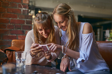 Open that. Cropped shot of two attractive young girlfriends looking at a cellphone while sitting in a cafe.