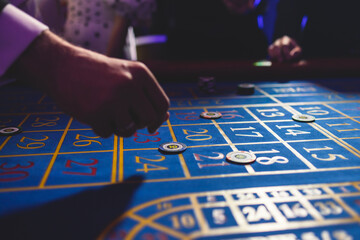 Naklejka premium Vibrant casino table with roulette in motion, with casino chips, tokens, the hand of croupier, dollar bill money and a group of gambling rich wealthy people playing bet in the background