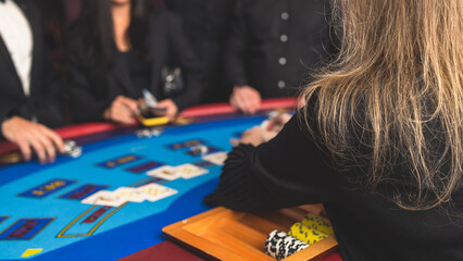 Fototapeta premium Poker table view with a pack of cards, tokens, alcohol drinks, dollar money and group of gambling rich wealthy people playing poker in casino, with croupier