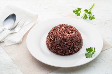 Cooked brown rice or riceberry rice on white plate on wood table