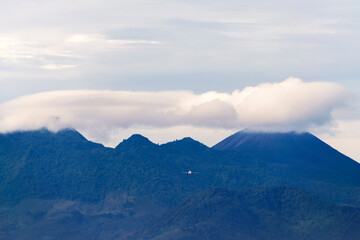 Panoramic view of Pacaya volcano and plane flying on a clear day with scattered clouds.