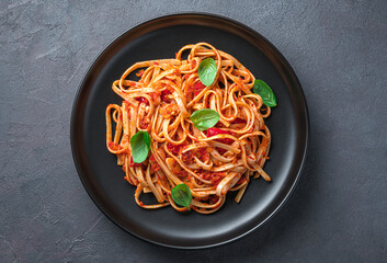 A portion of linguini pasta with tomatoes and basil in close-up on a gray-blue background. Italian...