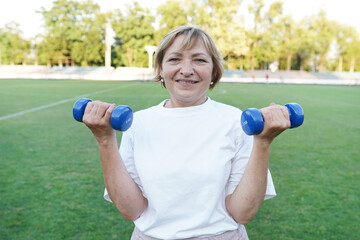 Mature woman exercising outdoors, doing dumbbell curls in the fresh air
