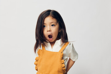 a cute little girl of preschool age is standing in an orange dress on a white background cheerfully...