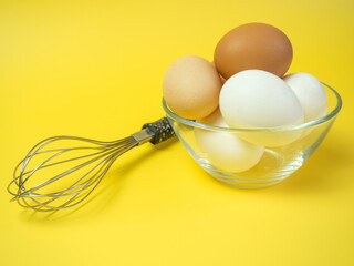 Top view of whisk and chicken eggs in glass bowl on yellow background,cooking concept