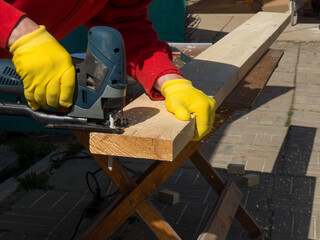 a man saws a board with an electric jigsaw close-up .hand electric saw ,the concept of working with...