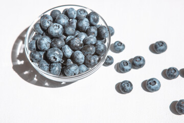 Blue blueberry in bowl and heap of berries on white table, card with fresh vegetarian food