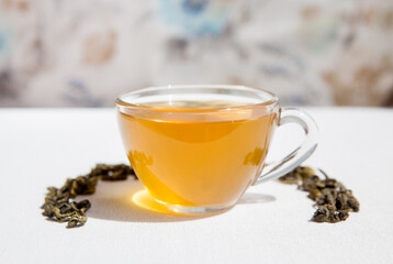 Glass cup of green tea with dry tea leaves on the table, card with hot drink