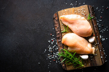 Chicken fillet with spices and herbs at wooden cutting board at black stone table. Raw meat and ingredients. Top view with copy space. © nadianb