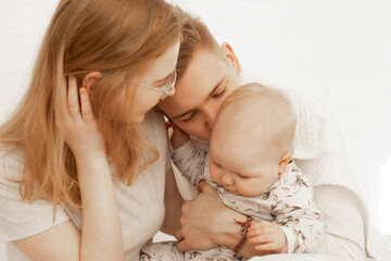 Young mother and father embrace little baby, have fun and enjoy on white background. Cute relationship between parents and infant child closeup, free copy space. Happy family and parental affection