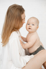 Young mother with little baby have fun and enjoy on white background. Portrait of happy woman and naked infant child closeup, free copy space. Concept of maternal affection and caring for children