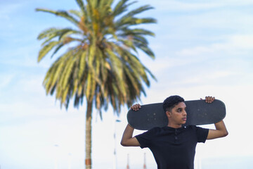 Selective focus: of a young Latin man posing with a skateboard in a park.