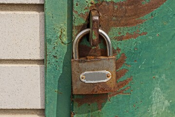 one gray metal padlock hangs on an iron green door in brown rust on the street