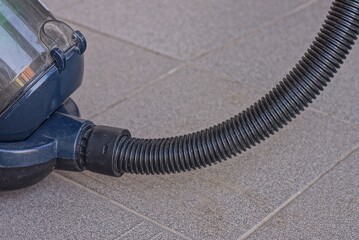 a long black plastic hose in a blue vacuum cleaner stands on a gray concrete floor