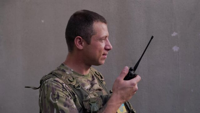 Ukrainian military man in army combat uniform with small Ukrainian flag using walkie-talkie