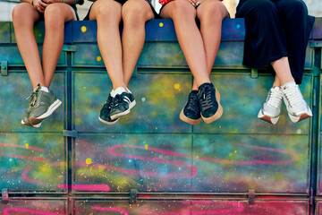 Take a seat. Cropped shot of four unrecognizable girlfriends sitting on a graffiti wall in the city.