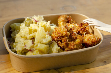 my lunch today outside, potato salad with cutlets on a paper tray on a wooden table	
