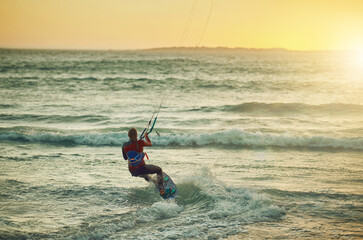 Riding waves makes for happy days. Rearview shot of a young woman kitesurfing at the beach.