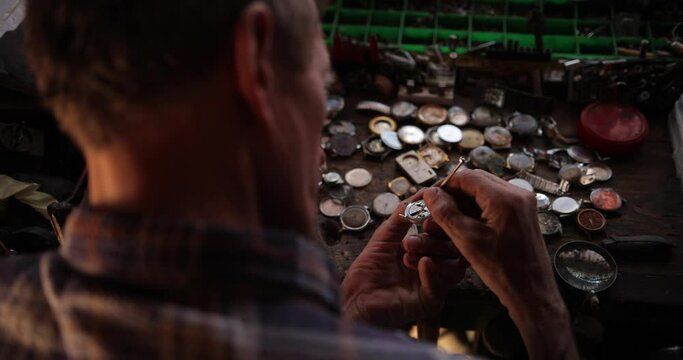 rear view of a professional watchmaker repairer working on a luxury mechanism watch gears in a workshop