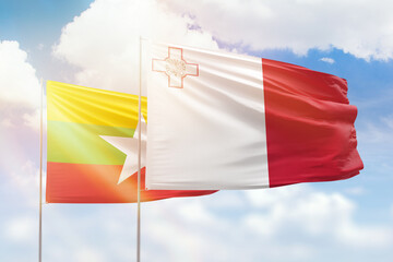 Sunny blue sky and flags of malta and myanmar