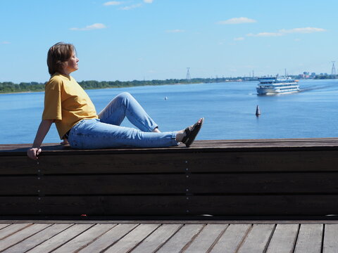  A girl is sitting on the pier, a cruise ship in the background.