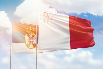 Sunny blue sky and flags of malta and serbia