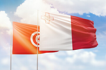 Sunny blue sky and flags of malta and tunisia
