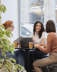 three female colleagues or students are working on a laptop and discussing a project or creative...