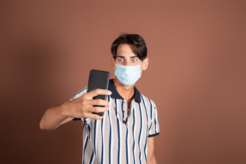 Emotional young man in a medical mask on a brown background. Medicine and diseases by airborne droplets.