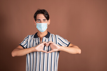 Emotional young man in a medical mask on a brown background. Medicine and diseases by airborne droplets.