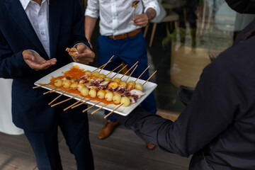 The waiter's hand, the waiter offers the dish to the guests. An appetizer at a feast, a wedding event, an appetizer on a plate on skewers, seafood dishes are chosen by guests.