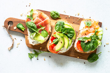 Open sandwich set with cream cheese, prosciutto, salmon, avocado and fresh greens. Top view at white table.