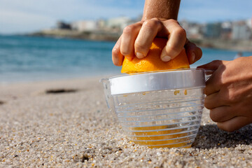 A woman's right hand holds half a juicy bright orange. The left hand holds the juicer. Squeezes the...