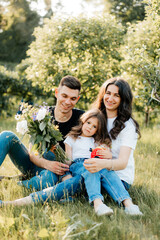 Beautiful young family with their daughter sits on the grass in the park