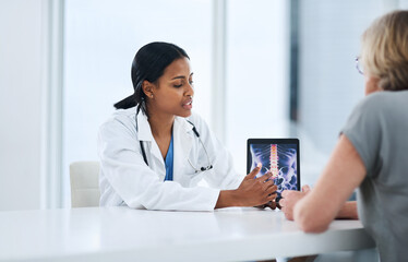 This is why youre feeling pain. Shot of a young doctor using a digital tablet during a consultation with a senior woman.