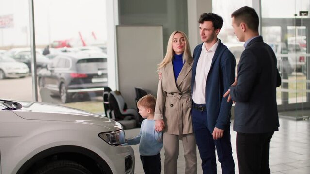 car dealership, joyful man and woman with a little boy choose a family automobile in dealership and consult with manager at sales center