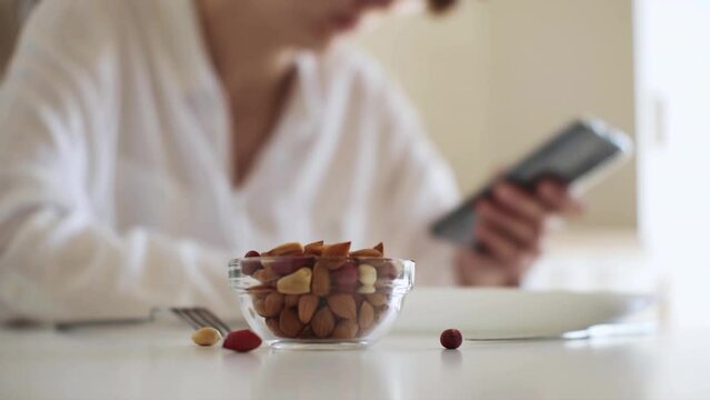 Peanuts on the table girl has breakfast looks into the phone eats high-calorie vegetarian food peanut nuts, Kitchen table white woman sits with a phone in her hands spending fun leisure time at home
