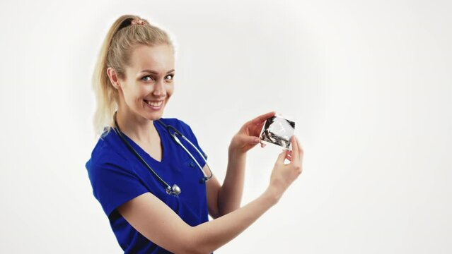 Young blond cheerful female gynecologist in blue uniform showing pregnancy USG picture to the camera over white background. High quality 4k footage