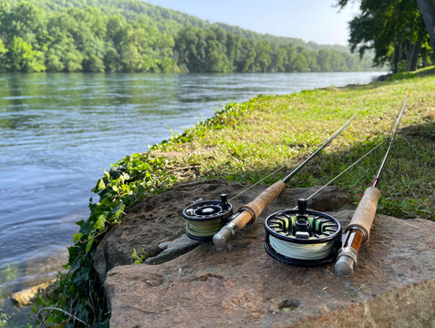 Two fly rods laying on the bank of a river on a summer day.