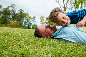 Sharing moments between father and son. Shot of a laughing father and son lying on grass.
