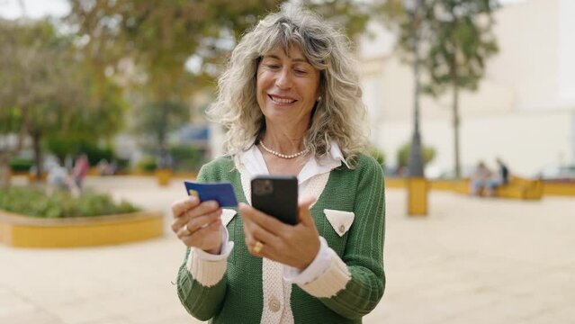 Middle age woman using smartphone and credit card at park