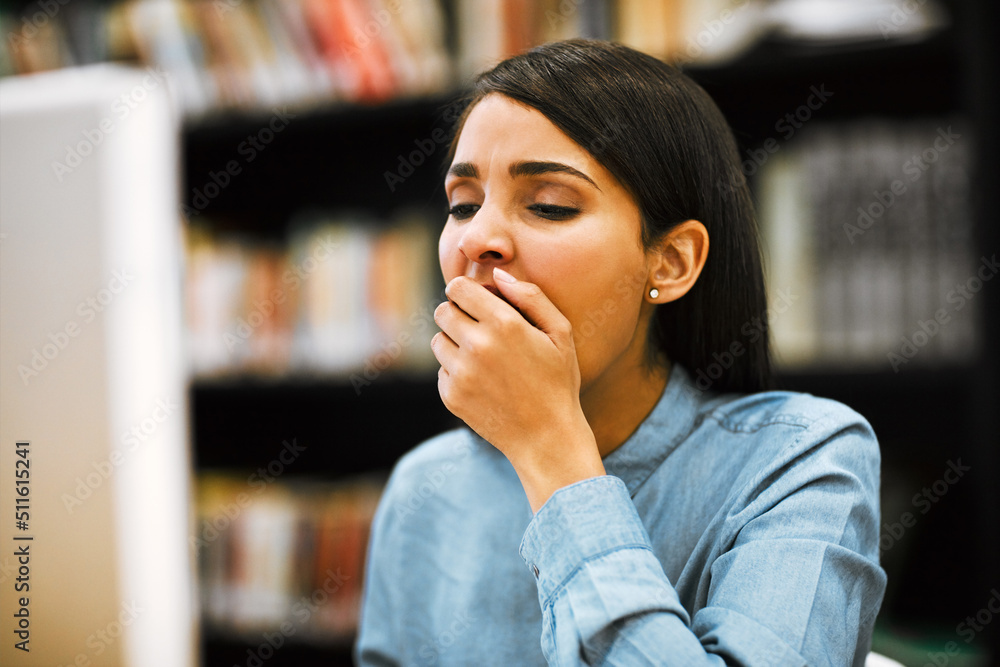 Fototapete The student life isnt all that easy to keep up with. Shot of a university student yawning while working on a computer in the library at campus.